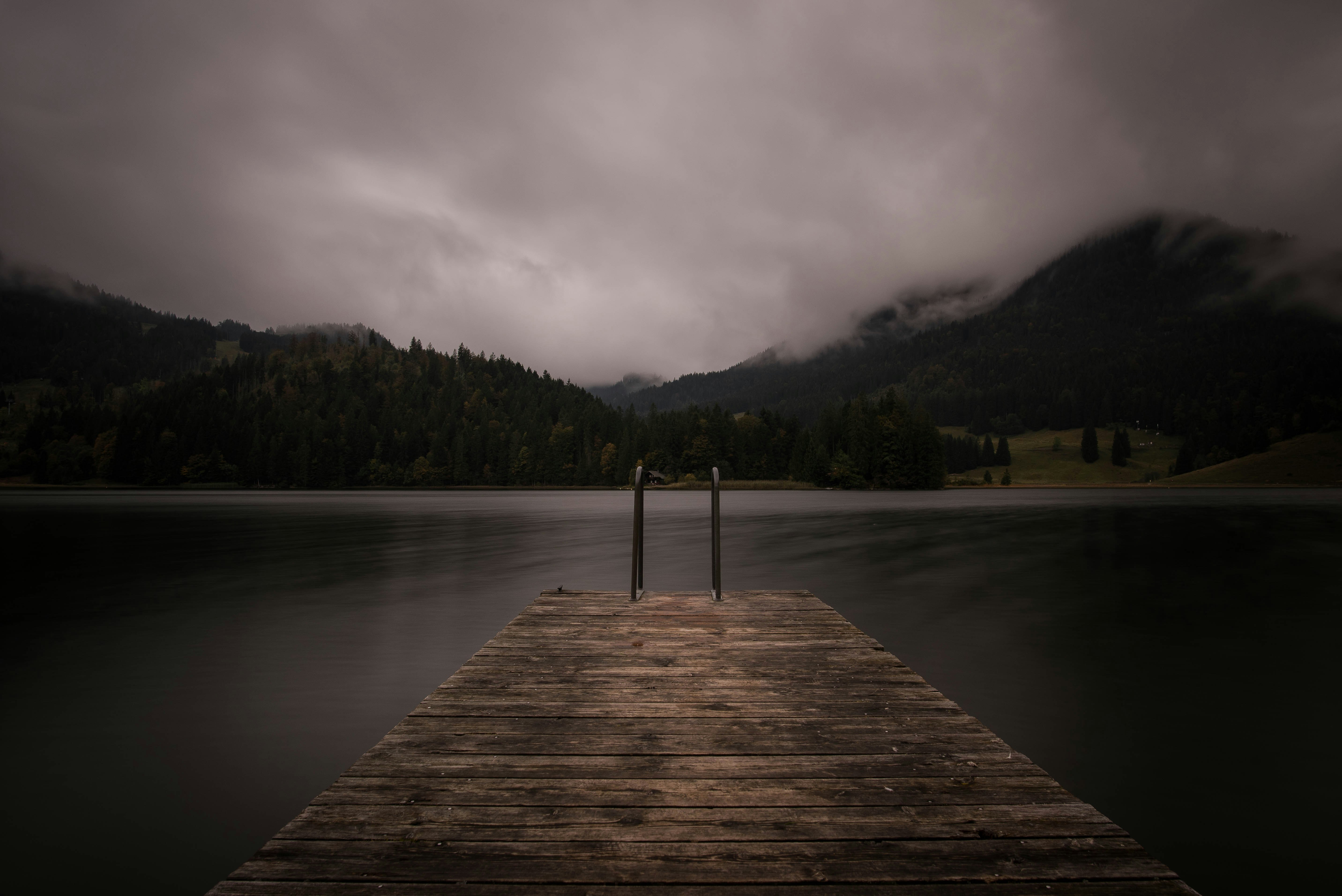 brown wooden dock near lake under cloudy sky
